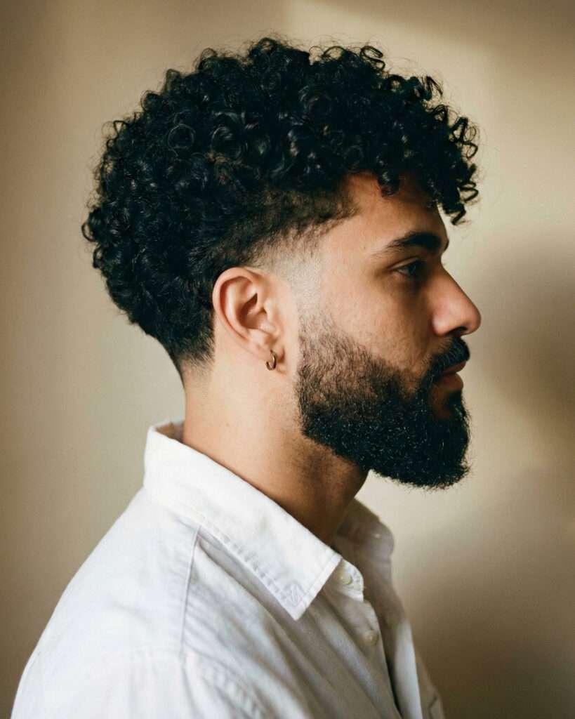Homem posando de lado com corte de cabelo taper fade com cachos no topo