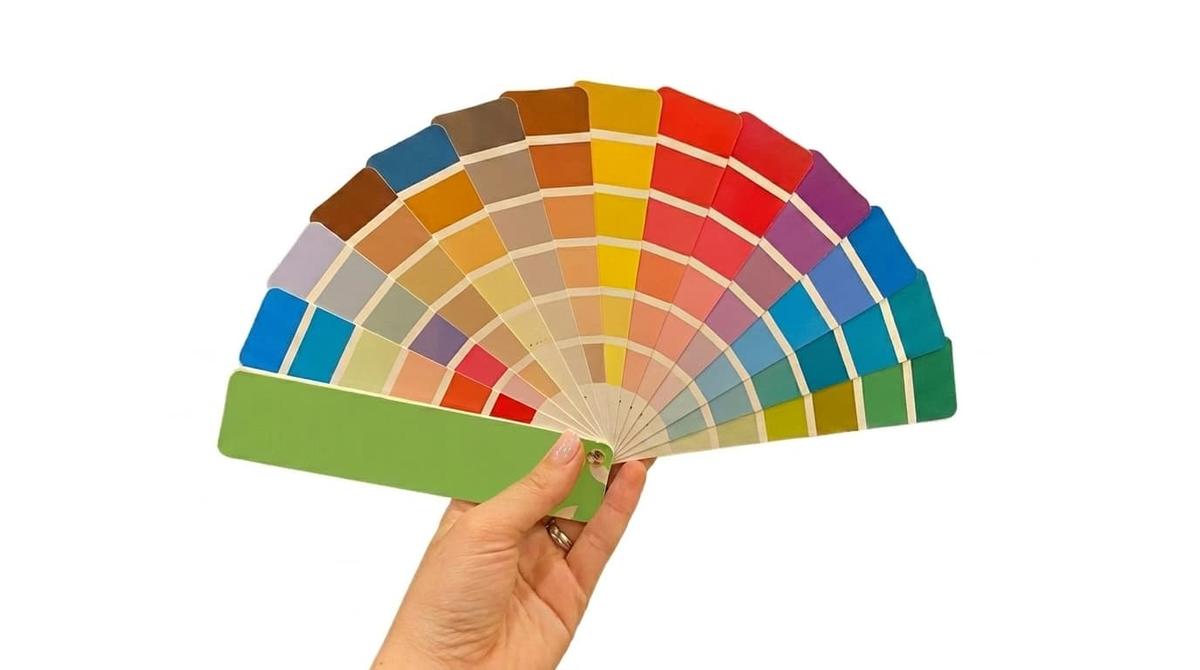 Mão segura leque aberto de amostras de cores variadas, tons pastéis a vibrantes, sobre fundo branco isolado.